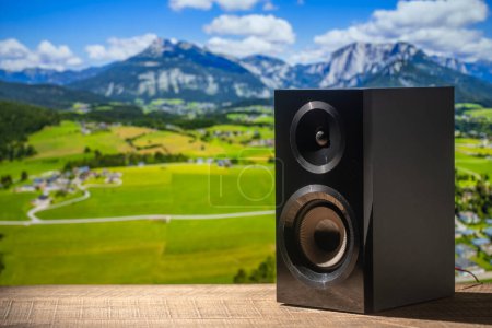 Photo for Black acoustic sound speaker on a wooden table against the backdrop of the Alpine mountains in Austria. The musical equipment, close up - Royalty Free Image