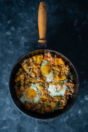Téléchargez les photos : Dans une casserole en fonte, fermez le riz bouilli avec des œufs frits, de la citrouille, des poivrons, des carottes et des oignons. Contexte alimentaire. Aliments sains - en image libre de droit