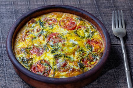 Photo for Ceramic bowl with vegetable frittata, simple vegetarian food. Frittata with egg, tomato, pepper, onion, green dill and cheese on wooden table, close up. Italian egg omelette - Royalty Free Image