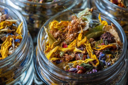Téléchargez les photos : Dry flower and herbal tea leaves in a glass jar on wooden background, copy space. Herbal collection of chamomile, cornflower, mint, sea buckthorn, lemongrass, wild rose, dried citrus fruits and apple - en image libre de droit