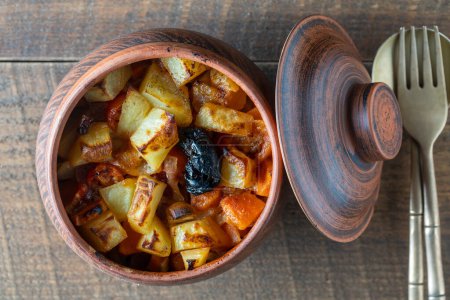 Photo for Stewed potato, carrot, onion, tomato and prunes in a clay pot on wooden table background, close up, top view - Royalty Free Image