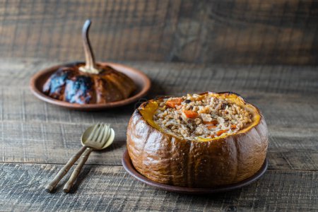 Photo for Great pumpkin baked with a filling close up. Stuffed roasted orange pumpkin, whole baked, filled with a tasty mixture of rice, raisins and spices on wooden table - Royalty Free Image