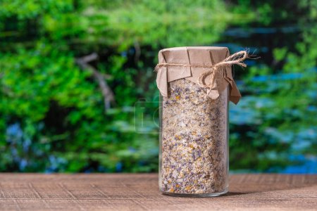 Photo for Sea himalayan salt with dry lavender and chamomile flowers in a glass jar on nature background on a sunny summer day, close up - Royalty Free Image
