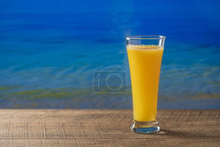 Photo for Freshly squeezed orange juice in glass on wooden table with sea water background on sunny summer day in tropical beach cafe, close up, copy space. Glass of fresh fruit orange juice. Vitamin C - Royalty Free Image