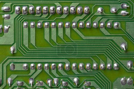 Photo for A part of a green printed circuit computer board with tracks. PCB without radio components. Old printed circuit board background with soldering trace, close up, top view - Royalty Free Image