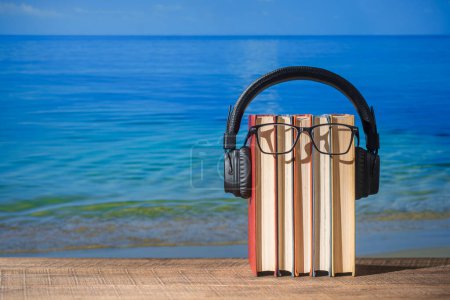 Foto de Conjunto de libros, auriculares y anteojos en mesa de madera cerca de agua de mar en la playa, de cerca. Audiolibros y concepto educativo - Imagen libre de derechos