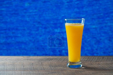 Téléchargez les photos : Jus d'orange fraîchement pressé en verre sur une table en bois avec fond d'eau de mer le jour d'été ensoleillé dans un café de plage tropical, fermer, copier l'espace. Verre de jus d'orange de fruits frais. Vitamine C - en image libre de droit