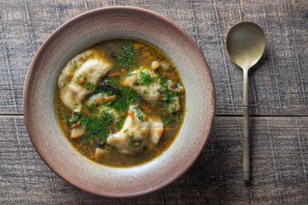 Photo for Mushroom soup plate with porcini mushrooms, dumplings, potato, carrot, onion, fresh green dill and pepper on black background, close up, top view - Royalty Free Image