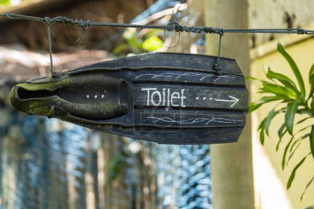 Photo for Black flippers with an inscription toilet in the form of a sign with a pointer, which is suspended on rope in a tropical beach cafe, close up, Thailand. Creative concept, the inscription - Royalty Free Image