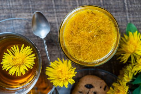 Photo for Sweet jam from ripe yellow petals of dandelion flowers, orange, lemon and sugar on the wooden table with tea and cookies, top view, close up - Royalty Free Image