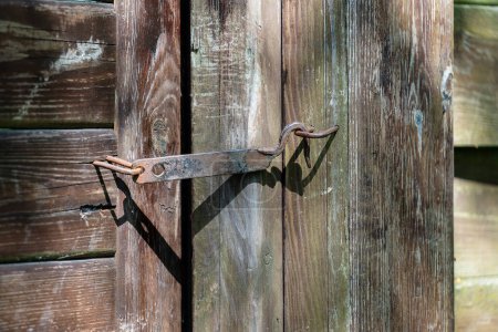 Photo for Wooden garden fence with a closed wicket door on a rusty old hook in the backyard, close up - Royalty Free Image