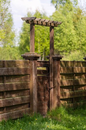 Téléchargez les photos : Clôture de jardin en bois avec porte fermée et herbe verte un jour de printemps à l'arrière-cour - en image libre de droit