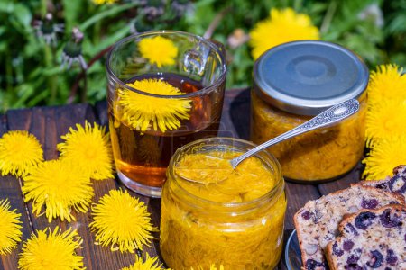 Photo for Healthy dandelion flower tea in a glass cup on the wooden table with sweet jam and cherry muffin in the spring garden, close up - Royalty Free Image