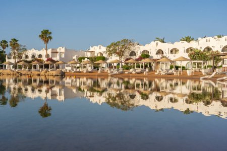 Foto de Edificios, tumbonas y sombrillas se reflejan en el tranquilo agua de mar en la playa en la ciudad turística de Sharm El Sheikh durante el amanecer, Egipto - Imagen libre de derechos