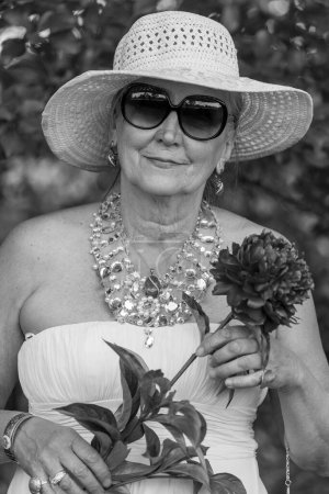 Foto de Retrato de una anciana feliz de 65 a 70 años con un sombrero de paja en el fondo de la naturaleza, de cerca. Blanco y negro - Imagen libre de derechos