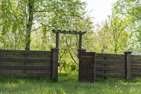 Téléchargez les photos : Clôture de jardin en bois avec porte ouverte et herbe verte un jour de printemps à l'arrière-cour - en image libre de droit