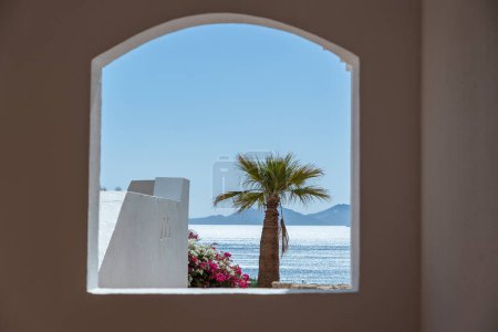 Téléchargez les photos : Trou de fenêtre dans le mur de pierre blanche d'un bâtiment donnant sur la mer Rouge et un palmier sur une plage tropicale dans la station balnéaire de Sharm El Sheikh, Egypte - en image libre de droit