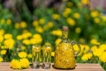 Photo for Homemade dandelion flowers tincture in two glasses and in a glass bottle on a wooden table in a summer garden, close up - Royalty Free Image
