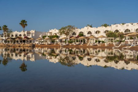 Foto de Edificios, tumbonas y sombrillas se reflejan en el tranquilo agua de mar en la playa en la ciudad turística de Sharm El Sheikh durante el amanecer, Egipto - Imagen libre de derechos