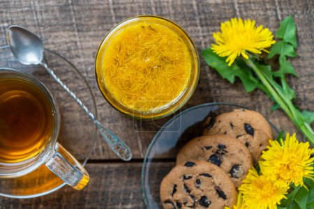 Photo for Sweet jam from ripe yellow petals of dandelion flowers, orange, lemon and sugar on the wooden table with tea and cookies, top view, close up - Royalty Free Image