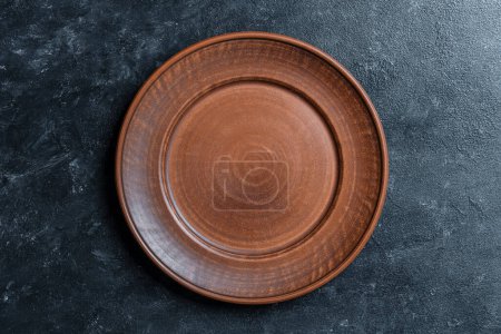 Photo for Empty flat plate of red clay over black background . Top view, close up . Rough ceramic bowl background with copy space - Royalty Free Image