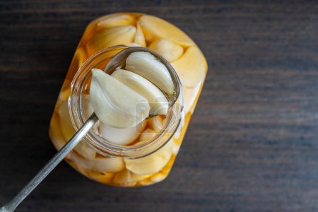 Photo for Spoon with sliced garlic cloves in honey over the opened honey jar, top view, close up, copy space. Honey infused garlic - Royalty Free Image