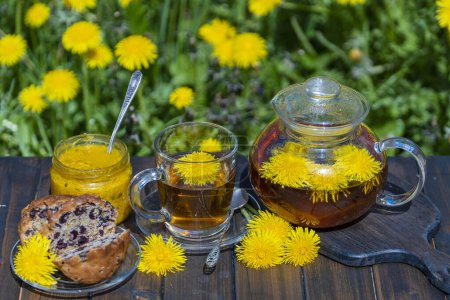 Photo for Healthy dandelion flower tea in a glass teapot on the wooden table in the spring garden, close up - Royalty Free Image