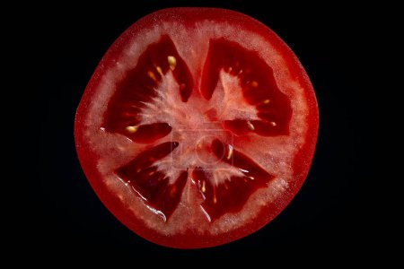 Foto de Rebanada de tomate rojo sobre fondo negro. Vista superior, primer plano, macro - Imagen libre de derechos