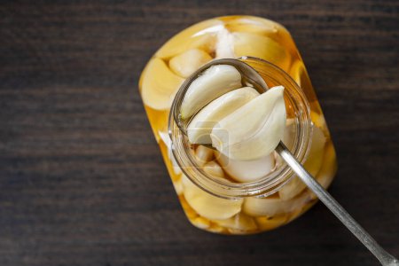 Foto de Cuchara con dientes de ajo en rodajas en miel sobre el frasco de miel abierto, vista superior, primer plano, espacio para copiar. Ajo infundido de miel - Imagen libre de derechos