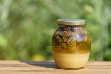 Photo for Glass jar of fresh honey with pine cones on a wooden table, close up - Royalty Free Image