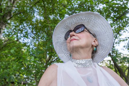 Téléchargez les photos : Portrait d'une heureuse femme âgée de 65 à 70 ans coiffée d'un chapeau de paille sur fond de nature, gros plan - en image libre de droit