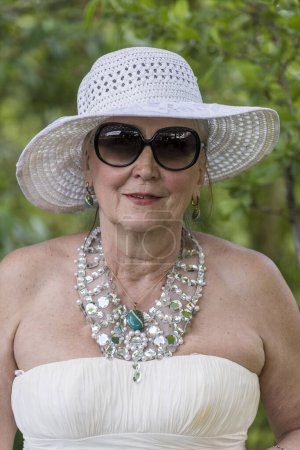 Foto de Retrato de una anciana feliz de 65 a 70 años en un sombrero de paja en el fondo de la naturaleza, de cerca - Imagen libre de derechos