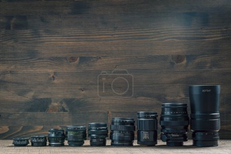 Photo for Set of vintage camera lenses from the times of the USSR on a wooden background, close up, copy space. Line of old retro lenses from small to large - Royalty Free Image