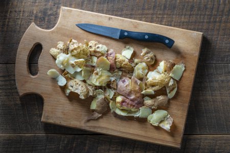 Téléchargez les photos : Pelure de pomme de terre bouillie sur une planche à découper en bois avec un couteau. Gros plan, vue du dessus. Peau de pomme de terre. Pommes de terre ingrédient de déchets organiques - en image libre de droit