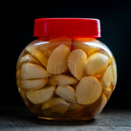 Foto de Cortar los dientes de ajo en rodajas de miel en frasco de vidrio, de cerca. Ajo infundido de miel - Imagen libre de derechos