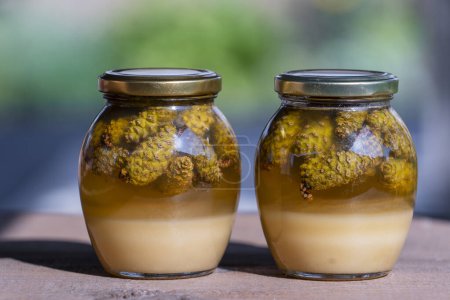 Foto de Dos tarros de vidrio de miel fresca con conos de pino en una mesa de madera, de cerca - Imagen libre de derechos