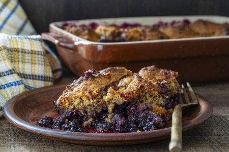Photo for Slice of fresh baked blueberry cobbler on white plate with fork. Homemade berry cobbler, close up - Royalty Free Image