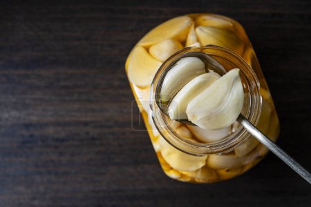 Foto de Cuchara con dientes de ajo en rodajas en miel sobre el frasco de miel abierto, vista superior, primer plano, espacio para copiar. Ajo infundido de miel - Imagen libre de derechos