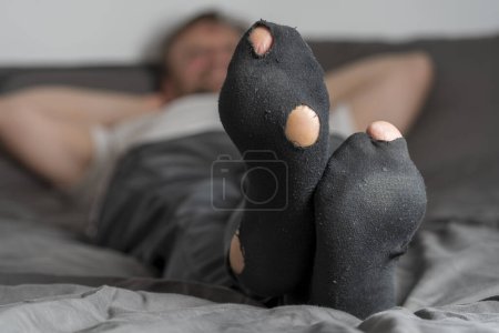 Foto de Hombre adulto con un agujero en los calcetines acostado en la cama, de cerca. Hombre con calcetines gastados relajante - Imagen libre de derechos