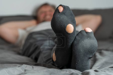Photo for Adult man with a hole in his socks lying in bed, close up. Man with worn out socks relaxing - Royalty Free Image