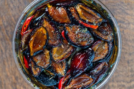 Prunes séchées au soleil avec ail, piment rouge, huile d'olive et épices dans un bocal en verre sur une table en bois. Style rustique, vue de dessus, gros plan