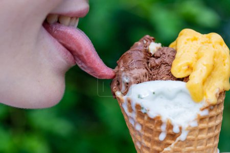 Foto de Chica joven lame helado en un cono con la punta de la lengua en el café de la calle al aire libre. Primer plano de los labios con helado a la hora del verano - Imagen libre de derechos
