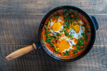Téléchargez les photos : Délicieux shakshuka aux œufs, tomate et persil dans une casserole en fonte, fermer, vue sur le dessus. Shakshuka - ragoût traditionnel de tomate israélienne aux œufs - en image libre de droit