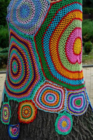 Photo for Colorful crochet knit on a tree trunk in Kyiv, Ukraine. Street art goes by different names, graffiti knitting, yarn bombing. Abstract background of knitted rugs with a multicolored circles pattern - Royalty Free Image