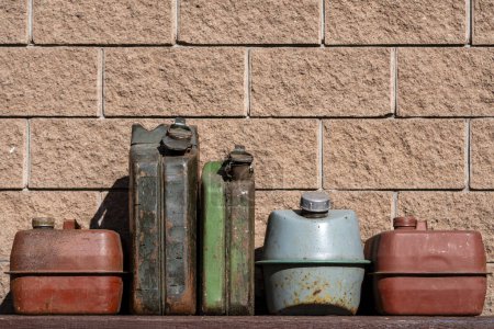 Foto de Muchas latas de hierro oxidado viejo combustible en una mesa cerca del garaje, de cerca. Varios recipientes pintados de metal para gasolina, estilo retro - Imagen libre de derechos