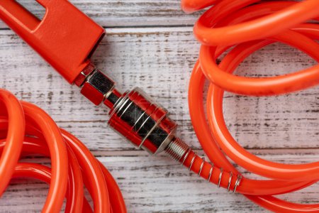 Téléchargez les photos : Un tuyau d'air orange avec un raccord de tuyau sur un fond en bois blanc, fermer. Détail du tuyau et du pistolet du compresseur d'air - en image libre de droit