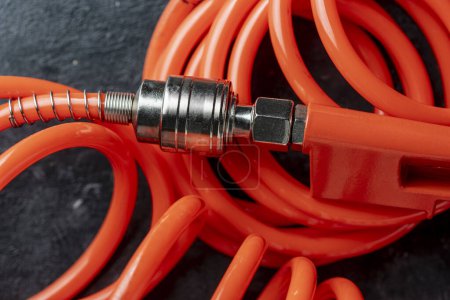 Téléchargez les photos : Un tuyau d'air orange avec un raccord de tuyau sur un fond noir, fermer. Détail du tuyau et du pistolet du compresseur d'air - en image libre de droit