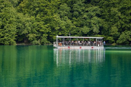 Foto de Plitvice Lakes, Croacia - 30 de agosto de 2021: La gente navega en un barco turístico a lo largo de la costa de Plitvice Lakes con bosque en verano en Croacia, Europa Central, viaje y concepto de naturaleza - Imagen libre de derechos