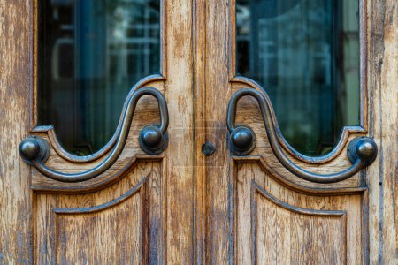 Photo for Dark old brown doors with bronze handles and glass. Wooden door with windows with street reflection, close up - Royalty Free Image
