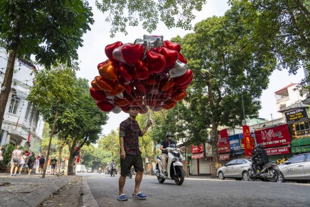 Photo for Hanoi, Vietnam - march 08, 2020 : Vietnamese seller offers to buy red heart shaped balloons on the street in the old town of Hanoi, Vietnam - Royalty Free Image